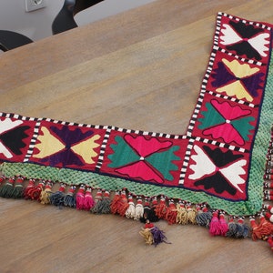 May include: A colorful embroidered fabric trim with a geometric pattern and tassels. The trim is made of red, green, white, black, and purple fabric. The tassels are made of various colors, including red, green, white, and black.