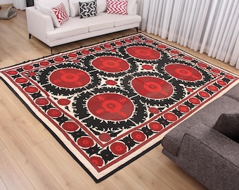 May include: Large, rectangular area rug with a bold, geometric design. The rug features a central pattern of large red circles on a black background, framed by a white border with red and black accents. The rug is placed on a hardwood floor.