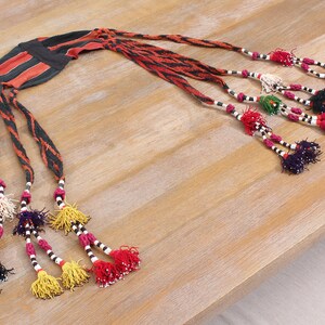 May include: A black and red woven headband with multiple beaded tassels in various colors, including white, black, red, yellow, green, and purple.