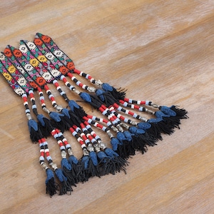 May include: A group of colorful, beaded tassels with black and blue fringe. The tassels are made with red, white, and black beads, and have a geometric pattern.