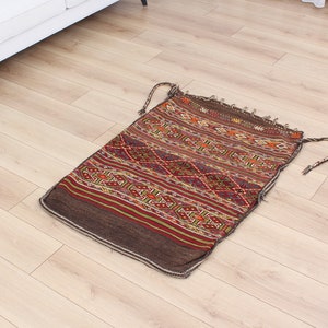 May include: A brown and red patterned rug with geometric designs. The rug has a fringed edge and is made of wool.