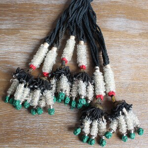 May include: A set of eight beaded tassels with black and white beads, green accents, and a black cord. The tassels are tied together at the top.