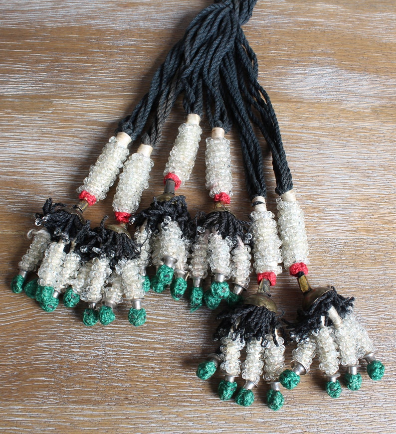 May include: A set of eight beaded tassels with black and white beads, green accents, and a black cord. The tassels are tied together at the top.