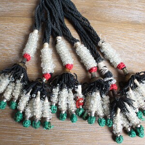 May include: A set of eight beaded tassels with black cords, white glass beads, red accents, and green tassels.