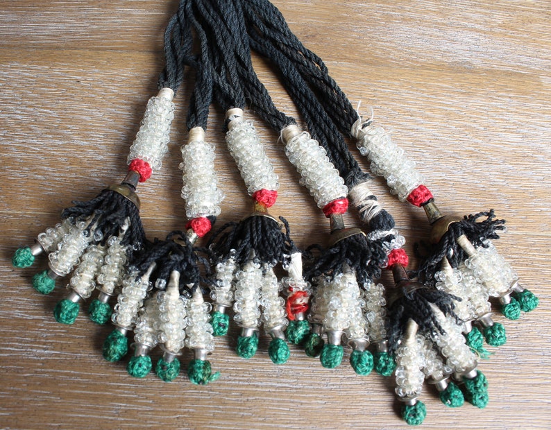 May include: A set of eight beaded tassels with black cords, white glass beads, red accents, and green tassels.
