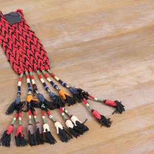 May include: A red and black woven tassel with beaded strands and black tassels. The tassel is made of a woven fabric with a geometric pattern.