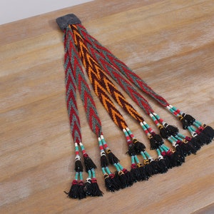 May include: A woven braid with multiple strands of red, orange, and green fabric, adorned with black tassels and turquoise, white, and red beads.