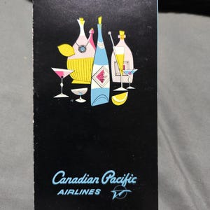 Może przedstawiać: Czarna, prostokątna okładka menu z grafiką przedstawiającą różne butelki koktajlowe, szklanki i cząstki cytryny. Napis "Canadian Pacific AIRLINES" jest wydrukowany jasnoniebieską czcionką na dole wraz z małym, okrągłym logo.