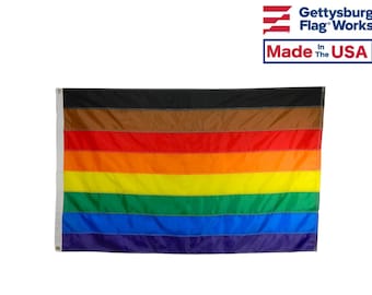 May include: A pride flag with eight horizontal stripes in the colors black, brown, red, orange, yellow, green, blue, and purple. The flag is made in the USA.