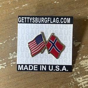 May include: A gold pin with two crossed flags. The flag on the left is the American flag, and the flag on the right is the Norwegian flag. The pin is on a white card with the text "GETTYSBURGFLAG.COM" and "MADE IN U.S.A."