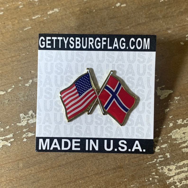 May include: A gold pin with two crossed flags. The flag on the left is the American flag, and the flag on the right is the Norwegian flag. The pin is on a white card with the text "GETTYSBURGFLAG.COM" and "MADE IN U.S.A."