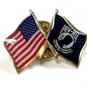 May include: A gold-colored pin with a crossed American flag and a POW MIA flag. The POW MIA flag is black with a white silhouette of a soldier's head and the words "POW MIA" and "You Are Not Forgotten".