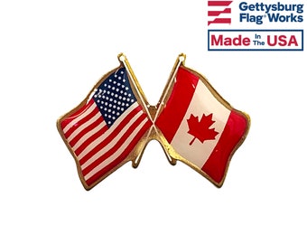 May include: A gold-colored pin with crossed American and Canadian flags. The American flag is red, white, and blue, and the Canadian flag is red and white with a maple leaf.