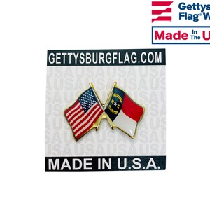 Puede incluir: Un pin de color dorado con dos banderas cruzadas. La bandera de arriba es la bandera estadounidense y la bandera de abajo es la bandera del estado de Carolina del Norte. El pin est&aacute; en una tarjeta blanca con el texto "GETTYSBURGFLAG.COM" y "MADE IN U.S.A."