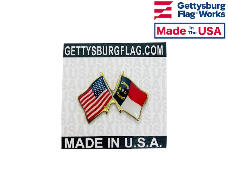 Puede incluir: Un pin de color dorado con dos banderas cruzadas. La bandera de arriba es la bandera estadounidense y la bandera de abajo es la bandera del estado de Carolina del Norte. El pin est&aacute; en una tarjeta blanca con el texto "GETTYSBURGFLAG.COM" y "MADE IN U.S.A."