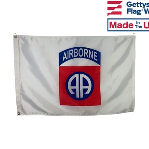 May include: A white flag with a red and blue patch. The patch has the words "AIRBORNE" in blue and a blue circle with the letters "AA" inside.