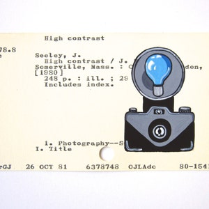 May include: A vintage library card with a black and white illustration of a camera with a flash. The text on the card reads "High contrast" and "Seeley, J. High contrast / J. Somerville, Mass.: [1980] 248 p. : ill. ; 29 Includes index."
