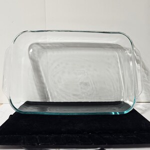 May include: A rectangular clear glass baking dish with rounded corners and integrated handles on both short sides. The transparent vessel features a smooth, polished surface and a deep interior basin, designed for oven use and food preparation.
