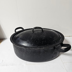 May include: A black oval-shaped cast iron Dutch oven with a matching lid. The pot features two side handles and a central handle on the lid. The exterior surface has a matte, textured finish with visible signs of wear and light gray scuffing.