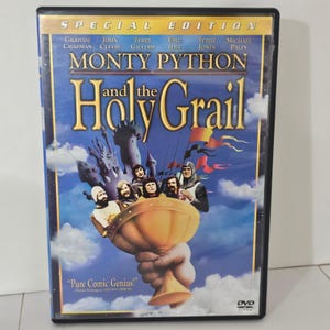 Può includere: Una custodia DVD Edizione Speciale del film Monty Python e il Sacro Graal. La copertina presenta un grande calice dorato tenuto da una mano gigante, con diversi membri del cast, un castello e bandiere colorate su un cielo blu con nuvole.