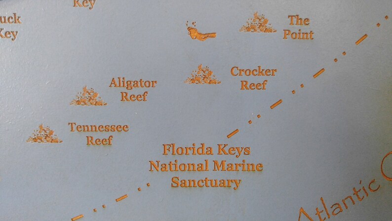 Puede incluir: Un mapa del Santuario Marino Nacional de los Cayos de Florida, que muestra las ubicaciones de Alligator Reef, Tennessee Reef, Crocker Reef y The Point. El mapa est&aacute; impreso en un fondo azul claro con texto naranja.
