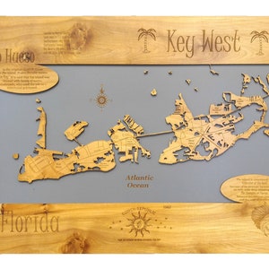 Puede incluir: Un mapa de madera de Cayo Hueso, Florida, con fondo gris. El mapa muestra las calles y los puntos de referencia de la isla. El texto "Key West" est&aacute; escrito en la parte superior del mapa, y el texto "Florida" est&aacute; escrito en la parte inferior. El mapa est&aacute; rodeado por un marco de madera.