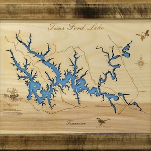 May include: Wooden framed map of Tims Ford Lake in Tennessee, with blue water detail. The map includes illustrations of wildlife, a compass rose, and the text "Tims Ford Lake". The frame is a dark brown color.