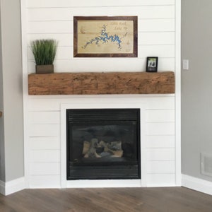 May include: A framed map of Table Rock Lake hangs above a rustic wooden mantel and a black fireplace. The map is printed on a light wood background with blue water and brown land features.
