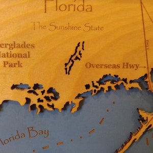 Puede incluir: Un mapa de madera de Florida con el texto "Florida, The Sunshine State" y "Everglades National Park" en el mapa. El mapa tambi&eacute;n muestra la Overseas Highway y la Bah&iacute;a de Florida.
