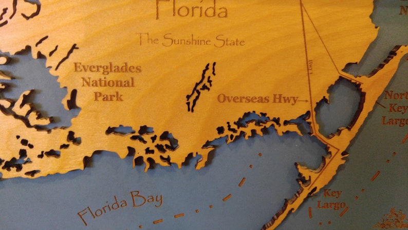 Puede incluir: Un mapa de madera de Florida con el texto "Florida, The Sunshine State" y "Everglades National Park" en el mapa. El mapa tambi&eacute;n muestra la Overseas Highway y la Bah&iacute;a de Florida.