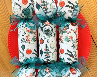 May include: Six Christmas crackers with a festive pattern of ornaments, holly, and Christmas trees. Each cracker is tied with a teal ribbon and sits on a red plate. The crackers are cylindrical and wrapped in white paper.