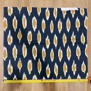 May include: A rectangular piece of fabric featuring a dark navy blue background with a repeating mustard yellow and white ikat-style diamond pattern. A yellow measuring tape is positioned along the bottom edge, showing a width of 26 inches.