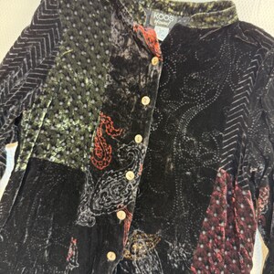 May include: A long-sleeve button-down shirt made of black velvet with a patchwork design. The garment features panels with varying textures, including chevron patterns, dotted sections, and paisley motifs in red and gold. A label reads KOOS of london.