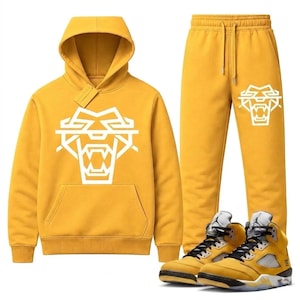 May include: A mustard yellow hooded sweatshirt with a large white geometric tiger head graphic on the chest, matching mustard yellow sweatpants with a smaller white tiger head graphic on the left leg, and high-top sneakers in mustard yellow.