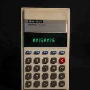 Puede incluir: Una calculadora vintage Sharp Elsi Mate EL-215 con cuerpo de plástico color hueso y un panel metálico plateado sobre la pantalla. La pantalla muestra una fila de ochos digitales verdes. Cuenta con una cuadrícula de botones de goma grises, azules y rojos.