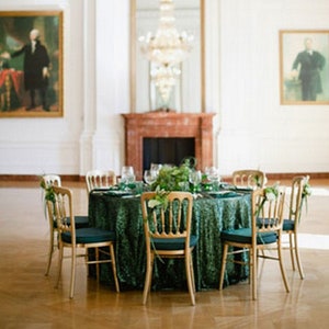 Op de afbeelding: Een formele eettafel met een groene fluwelen tafelkleed en gouden stoelen. De tafel is gedekt met witte borden, groene servetten en heldere glazen. Een grote kristallen kroonluchter hangt aan het plafond.