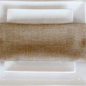 May include: Two white square plates stacked on top of each other with a brown burlap napkin on top of the plates.