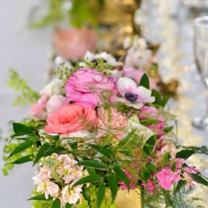 Puede incluir: Un arreglo floral en un jarr&oacute;n dorado con flores rosas, blancas y verdes. Las flores est&aacute;n dispuestas en un estilo moderno con vegetaci&oacute;n y helechos.