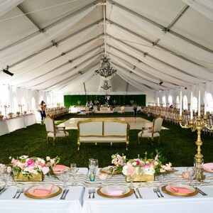 Puede incluir: Una carpa blanca con una pista de baile en el centro, decorada con manteles blancos, candelabros dorados y centros de mesa florales rosas. Las mesas est&aacute;n dispuestas con cargadores dorados, platos blancos y servilletas rosas.