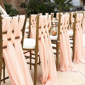 May include: A row of wooden chairs with light pink fabric sashes tied around the back of each chair. The sashes are tied in a decorative knot and drape down the back of the chairs.