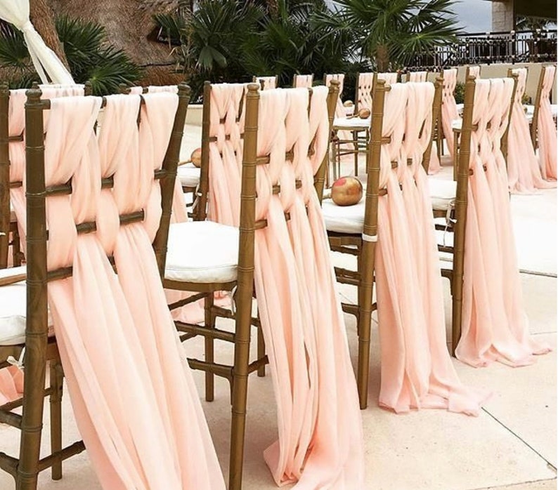 May include: A row of wooden chairs with light pink fabric sashes tied around the back of each chair. The sashes are tied in a decorative knot and drape down the back of the chairs.