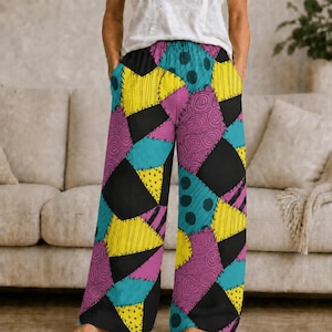 May include: Wide-leg lounge pants featuring a patchwork design of black, yellow, bright blue, and purple fabric segments. The pattern includes various textures like polka dots, swirls, and thin stripes, all connected by black stitched seam details.