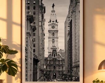May include: A framed black and white photograph of Philadelphia City Hall, featuring the iconic clock tower and statue of William Penn, centered between tall urban buildings, displayed in a vertical orientation with a dark wood frame.