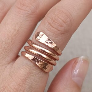 May include: A copper-coloured wrap ring featuring a multi-coil design that spirals around the finger. The metal band displays a hammered, textured finish on the two outer ends, while the two inner coils remain smooth and polished in appearance.