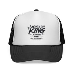 May include: A white and black trucker cap featuring a black graphic on the front panel. The design includes a crown icon, the text CAROLINA KING CUSTOMS, a small fish silhouette, and the text BUILT FOR THE ANGLER in a bold, stylised font.