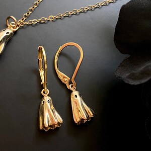May include: A gold necklace and earrings set featuring a ghost design. The necklace has a delicate chain and the earrings are dangle style.
