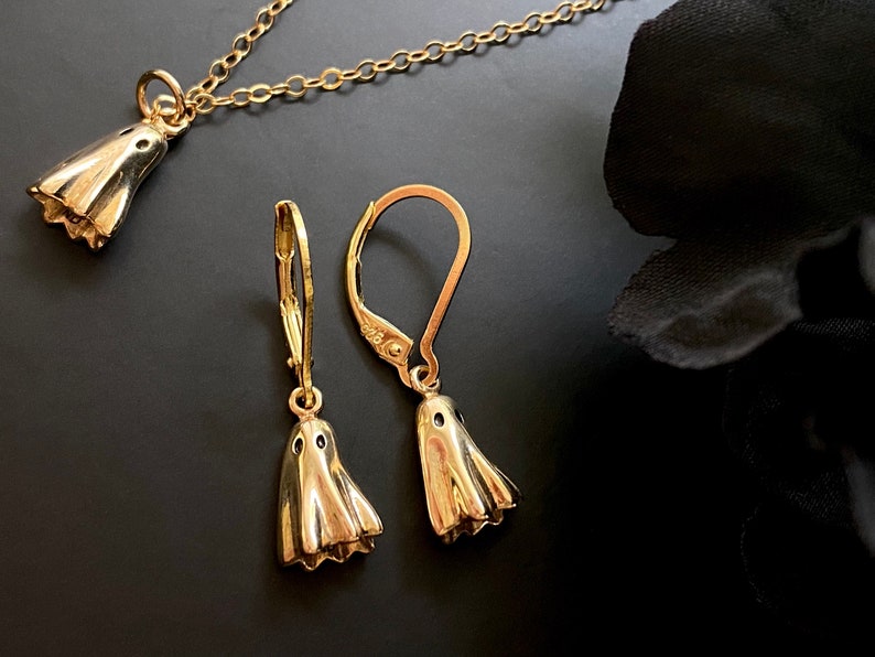 May include: A gold necklace and earrings set featuring a ghost design. The necklace has a delicate chain and the earrings are dangle style.