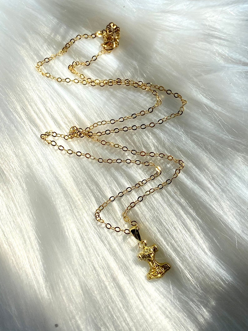 May include: A gold chain necklace with a small gold pendant shaped like a hammer.