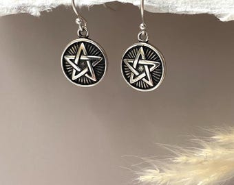 May include: A pair of silver-toned earrings. Each earring features a circular pendant with a raised pentagram design. The pentagram is surrounded by a sunburst pattern. The earrings have a simple hook closure.