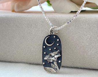 May include: A silver necklace with a pendant featuring a crescent moon and a flower with a starry background.